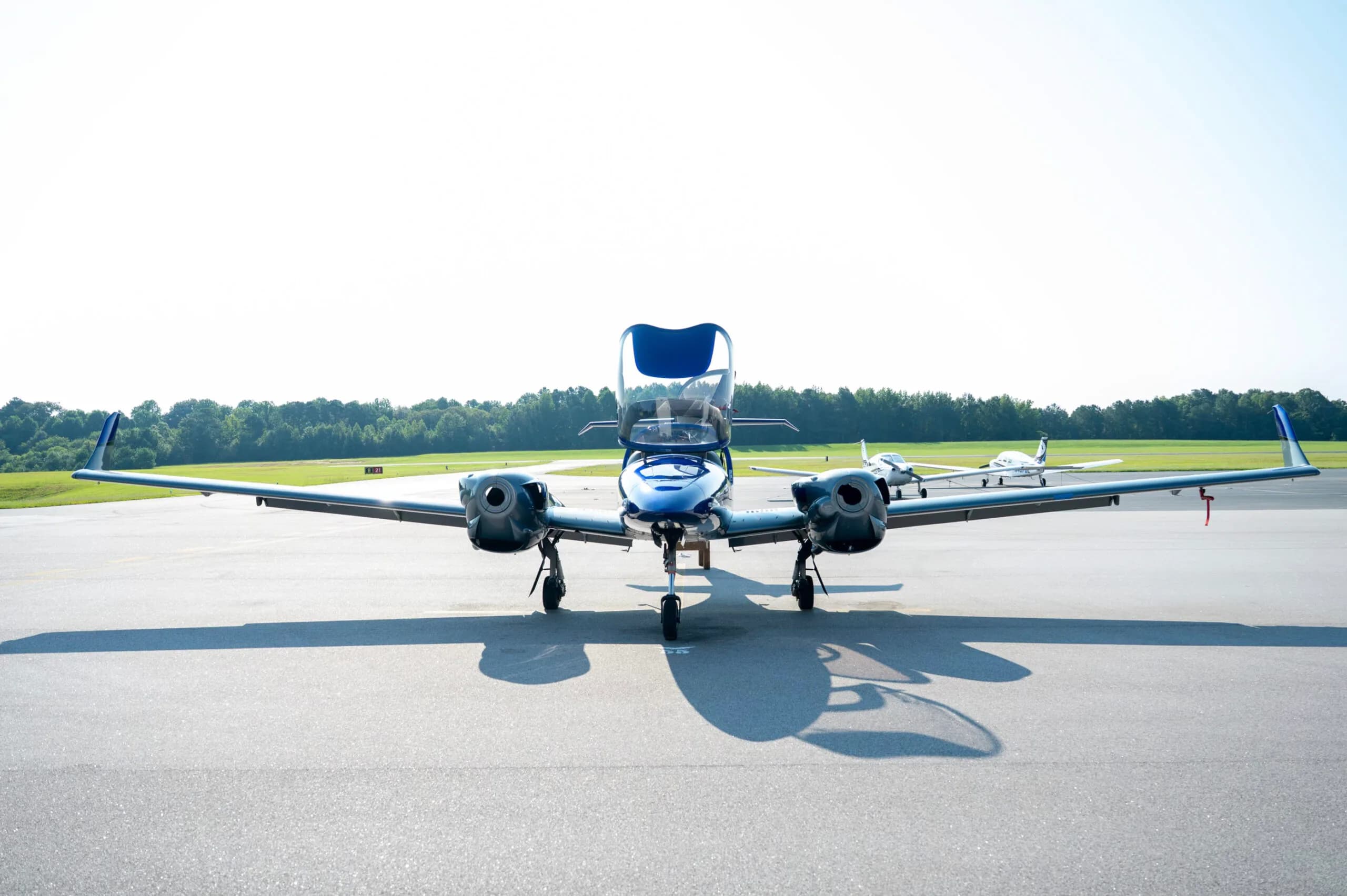Front view of a blue and grey Diamond DA42 aircraft with doors open, parked on an airfield.
