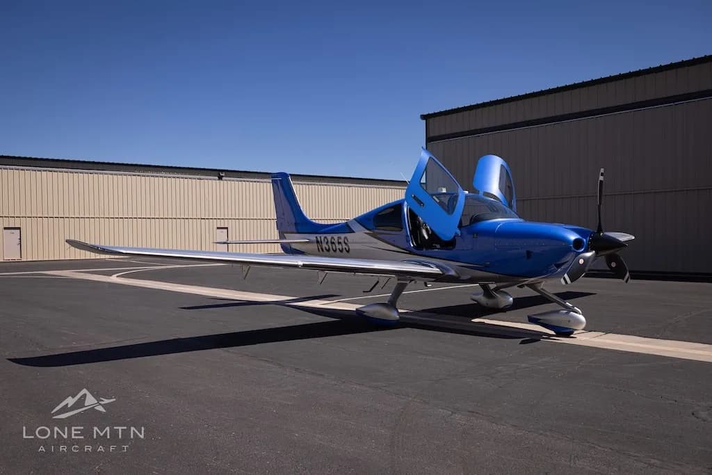 A front three-quarter view of the blue and silver Cirrus SR22 aircraft, N365S, with its doors open, parked on an asphalt ramp.
