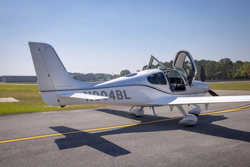 A side view of the silver Cirrus SR22 aircraft N904BL with its doors open, parked on an airfield.