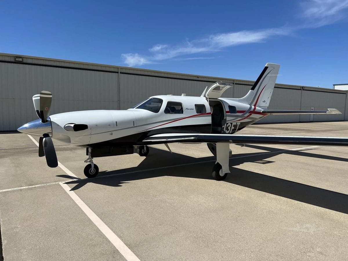 Side view of a Piper Meridian aircraft with the door open, parked on the tarmac.