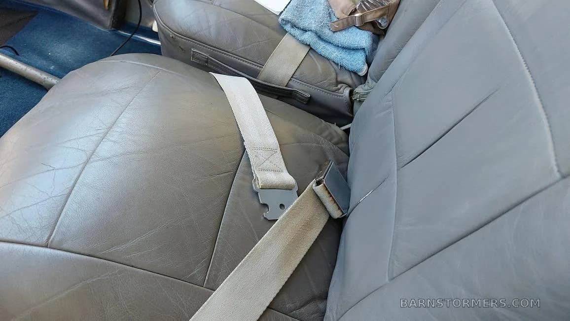 The gray leather seats and seatbelts in the aircraft cabin.