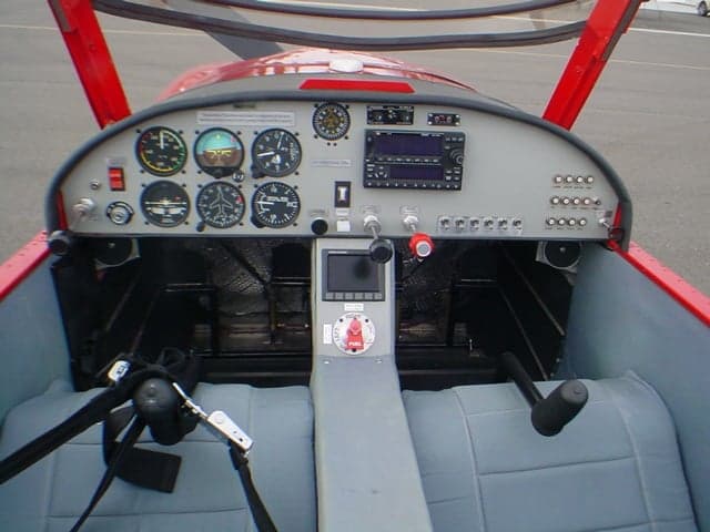 The cockpit of a light sport aircraft, showing the instrument panel, controls, and two grey seats.