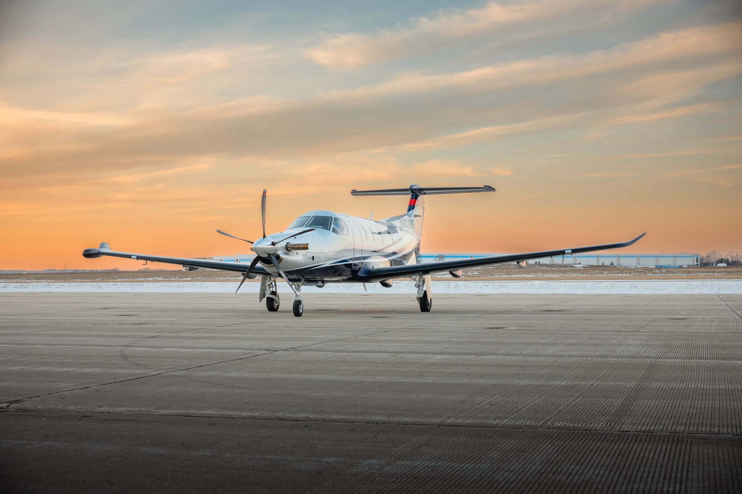 A silver and blue Pilatus PC-12 turboprop aircraft with tail number N882RR is parked on a tarmac under a sunrise sky.