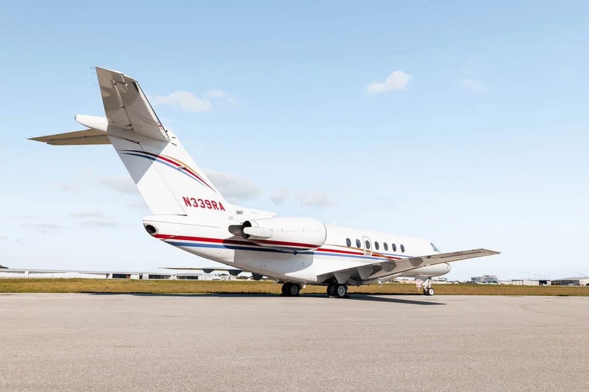 The rear-side view of a white Hawker 800XP business jet with red and blue stripes, registration N339RA, parked on the tarmac.