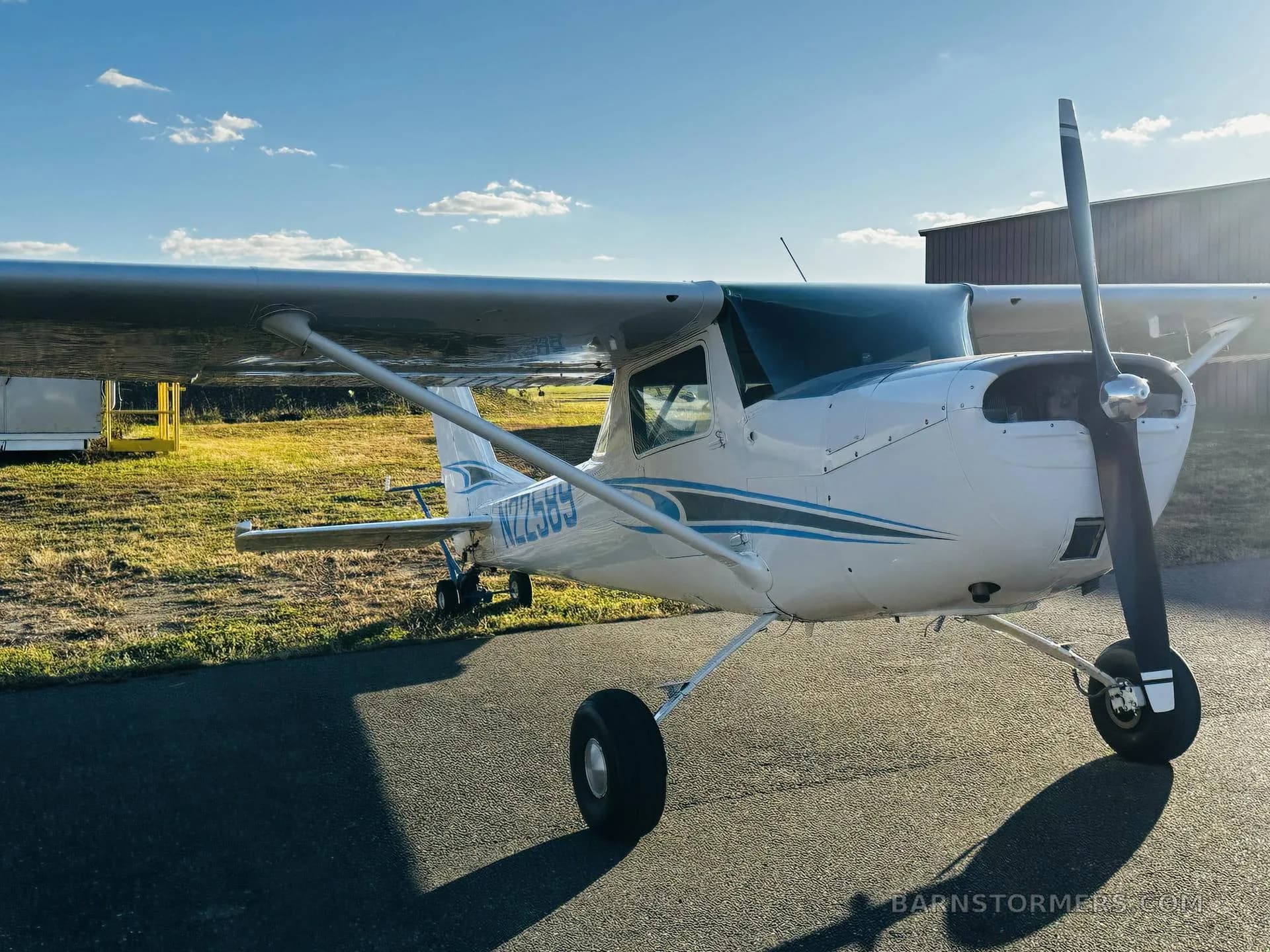 A front-quarter view of a white Cessna 150/152 type aircraft with blue and grey stripes, tail number N22589, parked on an asphalt ramp.