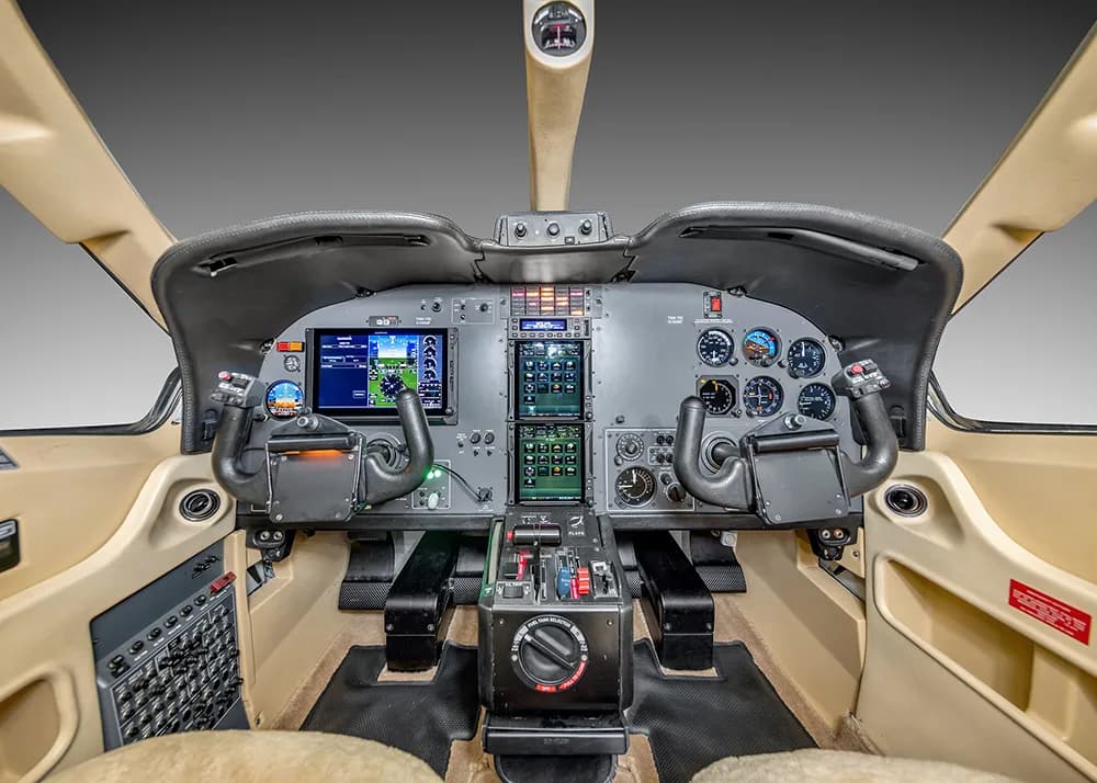 A detailed view of the TBM 900 series aircraft cockpit, featuring the instrument panel, dual yokes, and central controls.