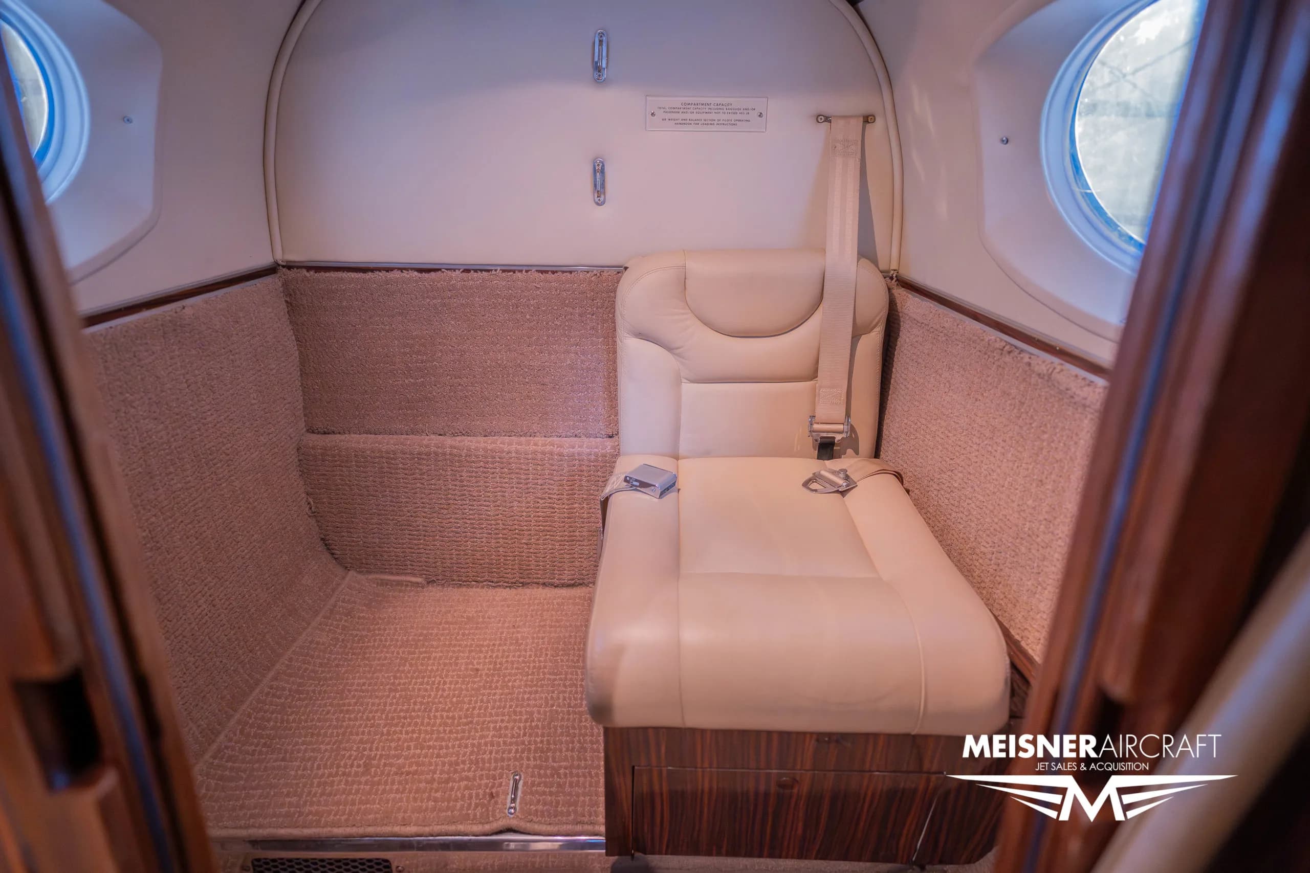 A single beige leather seat in the rear of the aircraft cabin, with carpeted walls.