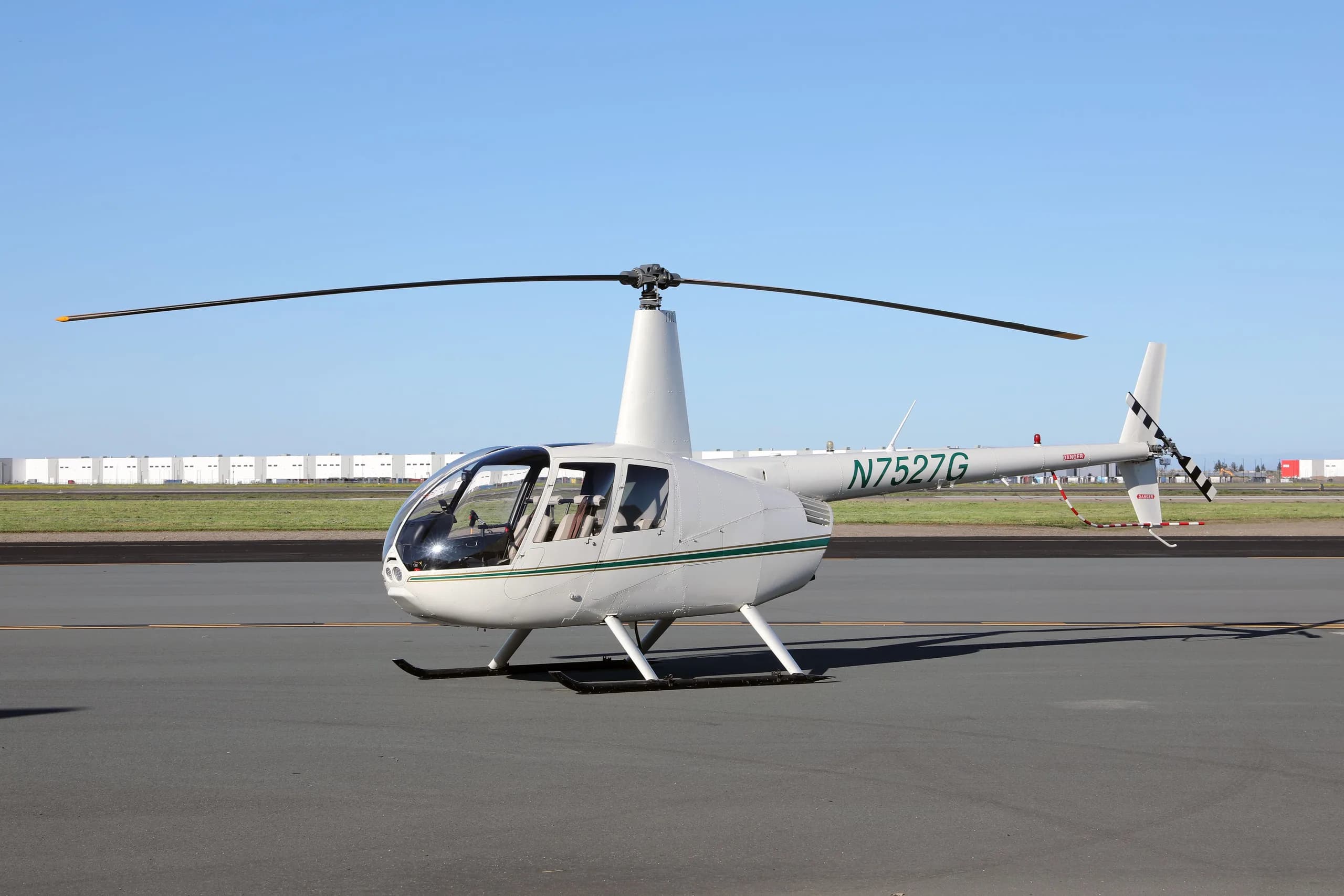 White Robinson R44 Raven II helicopter with a green stripe, registration N7527G, parked on an airfield.