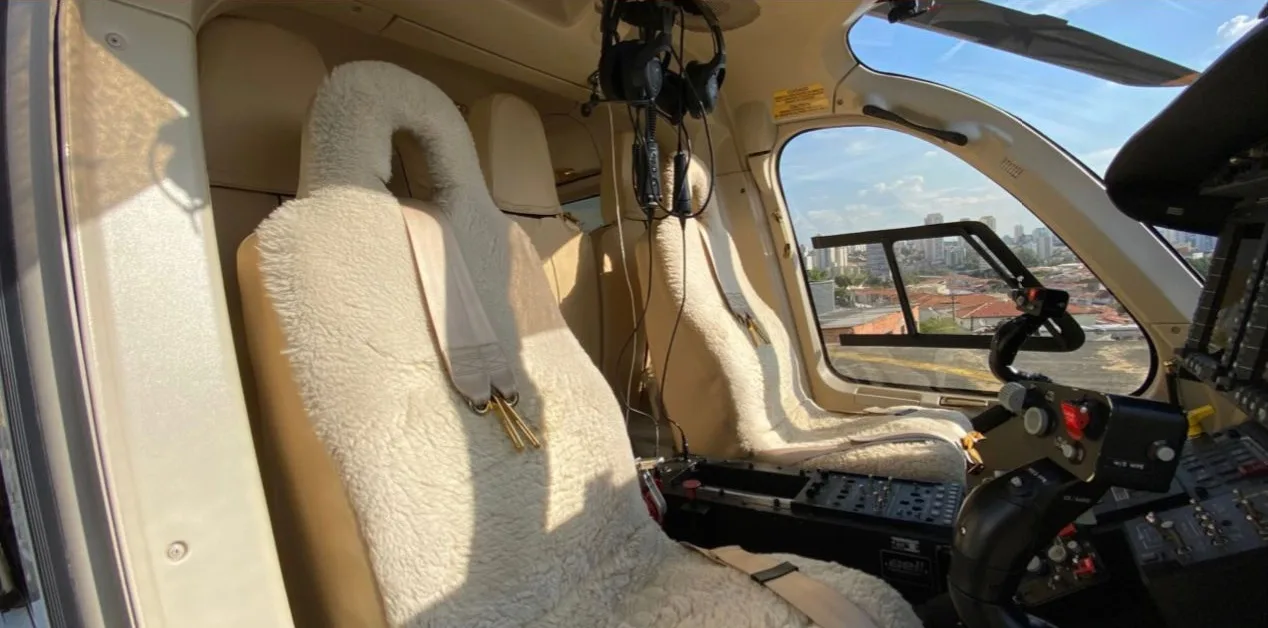 The front cabin seats of a helicopter, covered in white fluffy material, with a view of the city outside.