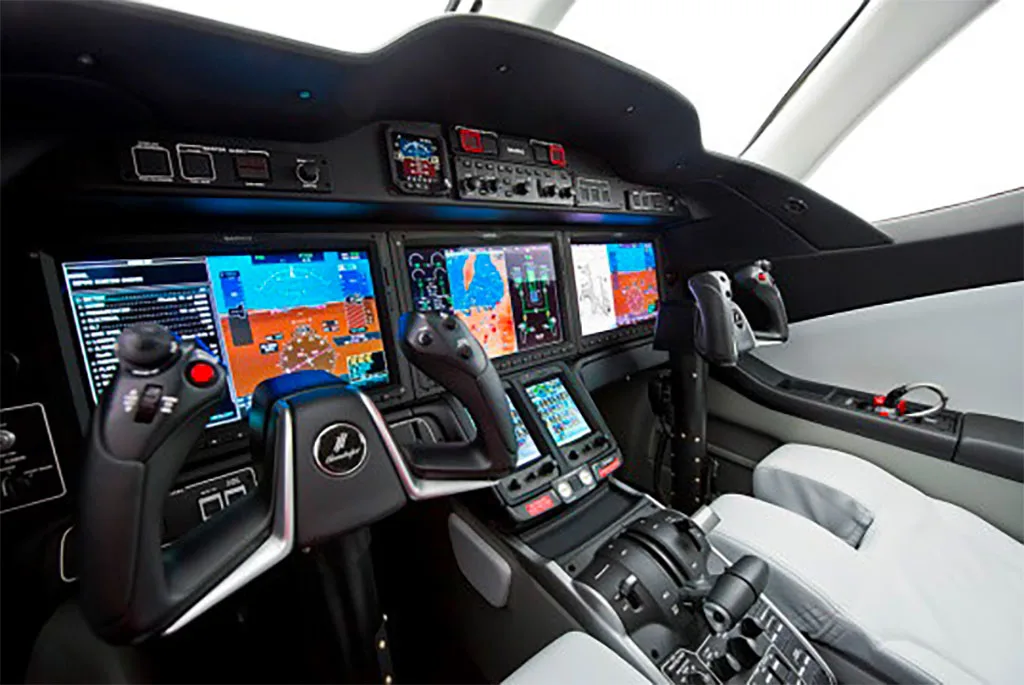 The advanced glass cockpit of a HondaJet with multiple large display screens and side-stick controls.
