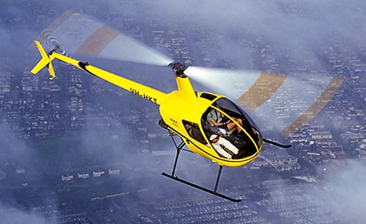 Robinson R22 Beta II helicopter flying near a mountain.