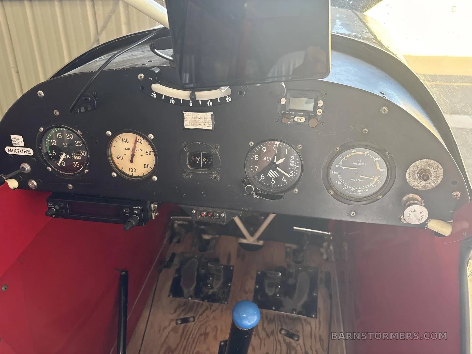 The cockpit instrument panel of a Piper Super Cub, showing analog gauges, a radio, and rudder pedals.