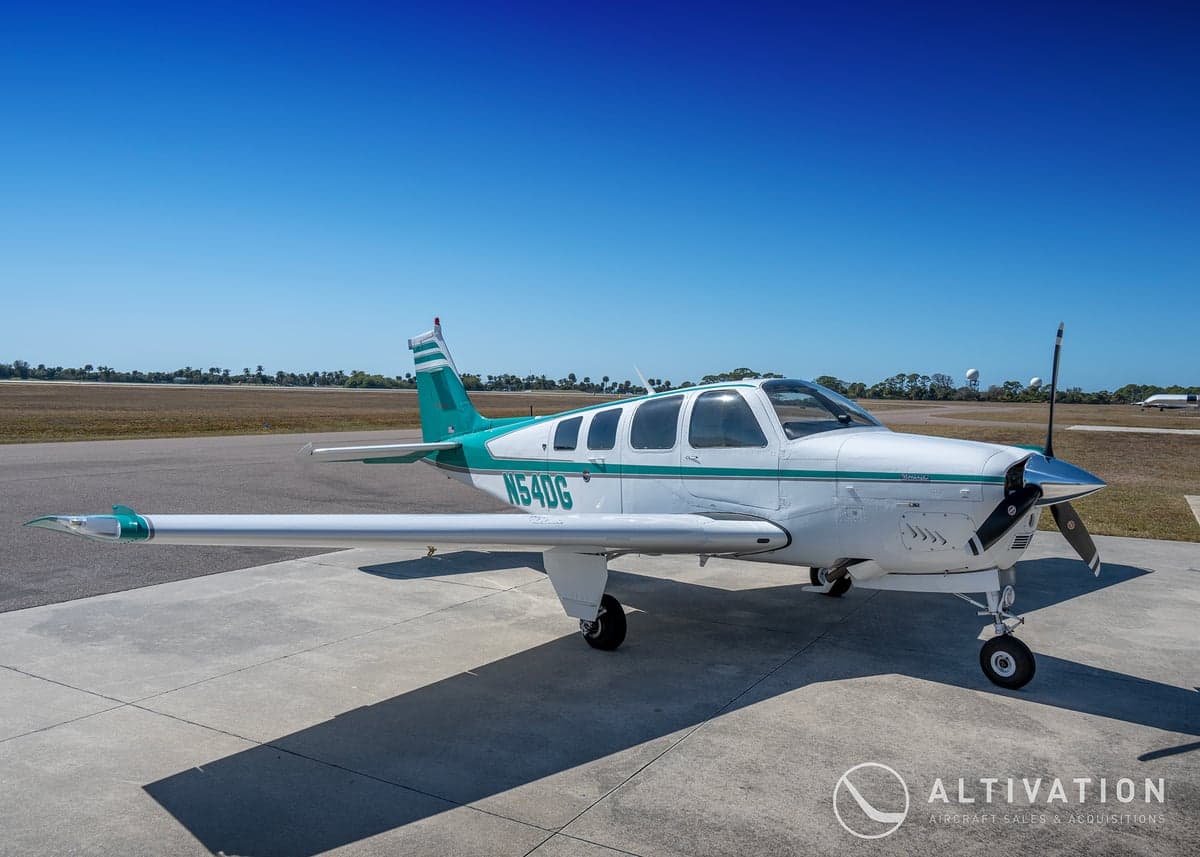 A Beechcraft Bonanza with a white and green paint scheme on the tarmac.