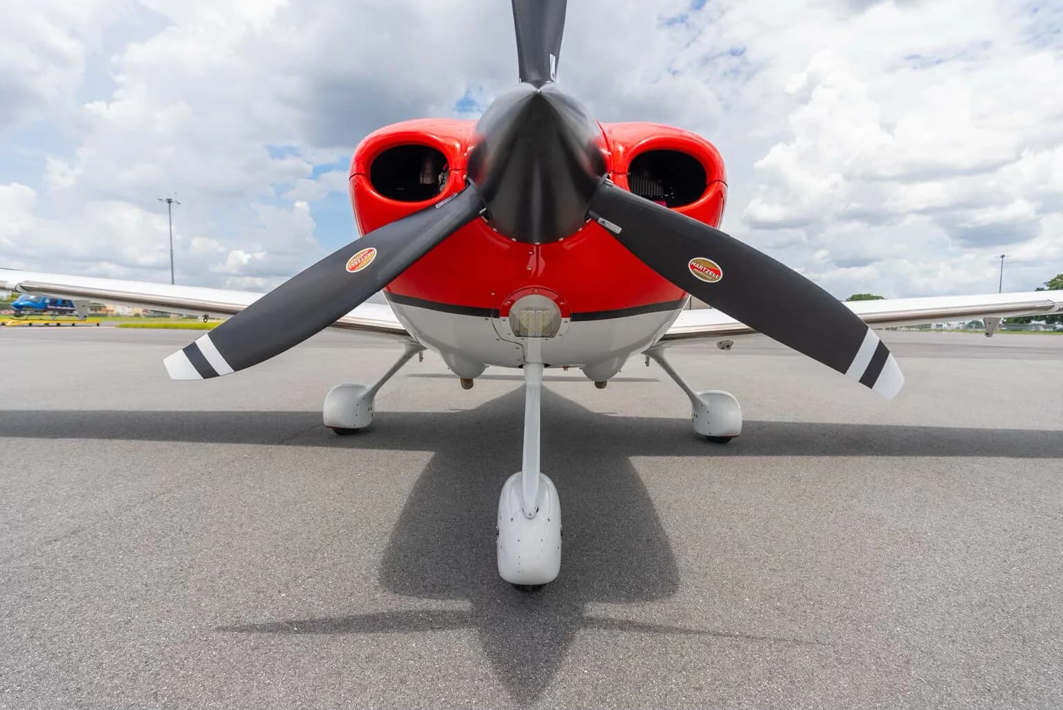 A head-on view of the red and white Cirrus SR22 aircraft, highlighting its propeller and nose landing gear.