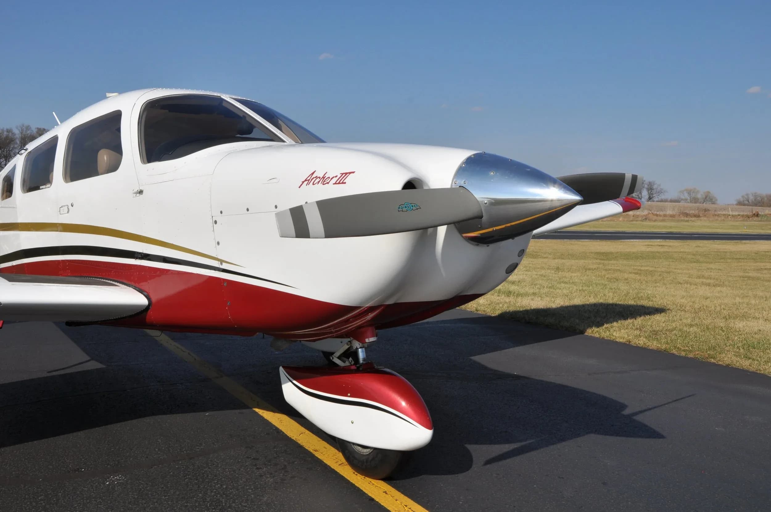 Close-up of the front of a Piper Archer III aircraft with a white and red paint scheme.