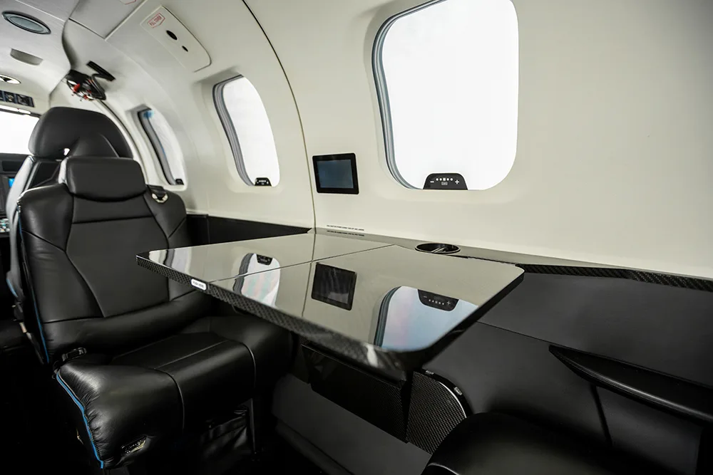 The aircraft cabin interior showing a black fold-out table and black leather seats.
