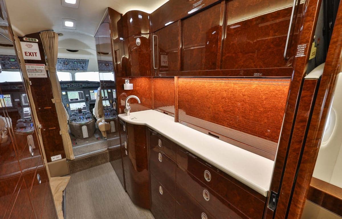 View of the aircraft interior showing a sink and cabinets, with a glimpse into the cockpit.