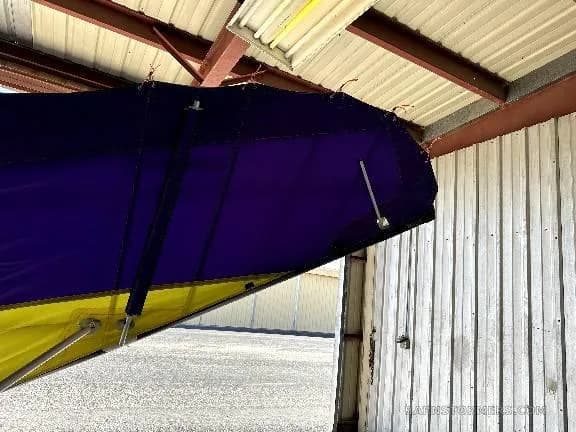 A close-up detail of the purple and yellow fabric wing of an aircraft, showing its structure.