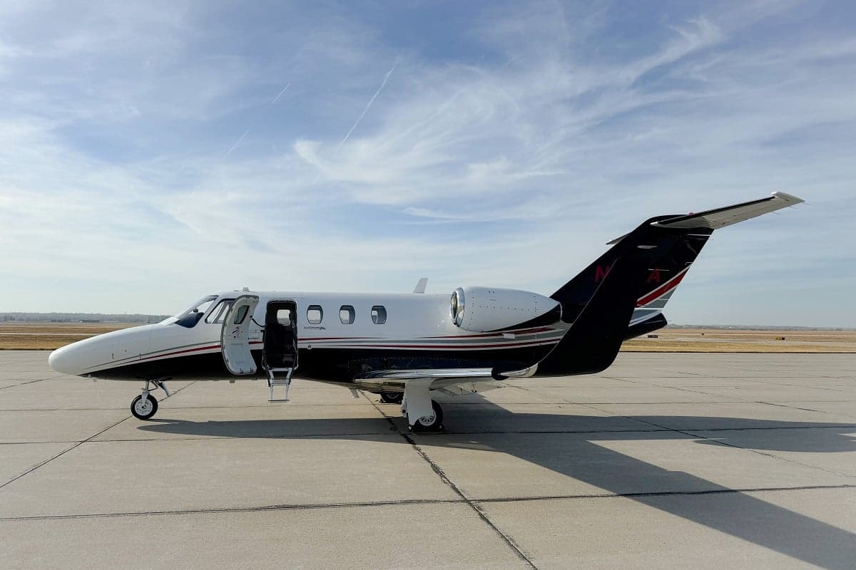 A Cessna Citation CJ3+ aircraft with an open door is parked on the tarmac.