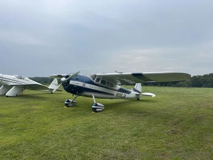 A blue and white Cessna 195 parked on a grassy field.