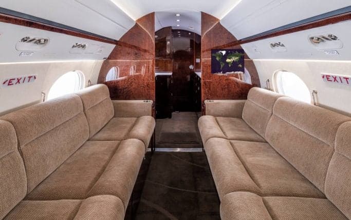 The interior cabin of a Gulfstream G450 aircraft with tables, seats, and a monitor.