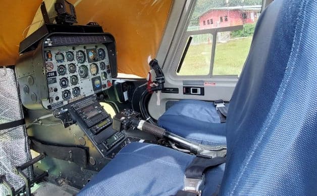 Helicopter cockpit with blue seats and instrument panel.
