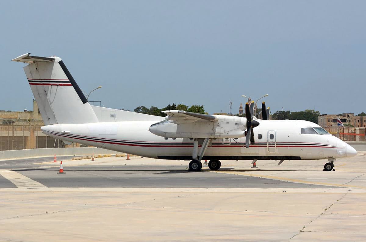 A side view of a white and red striped De Havilland Dash 8 on the tarmac.