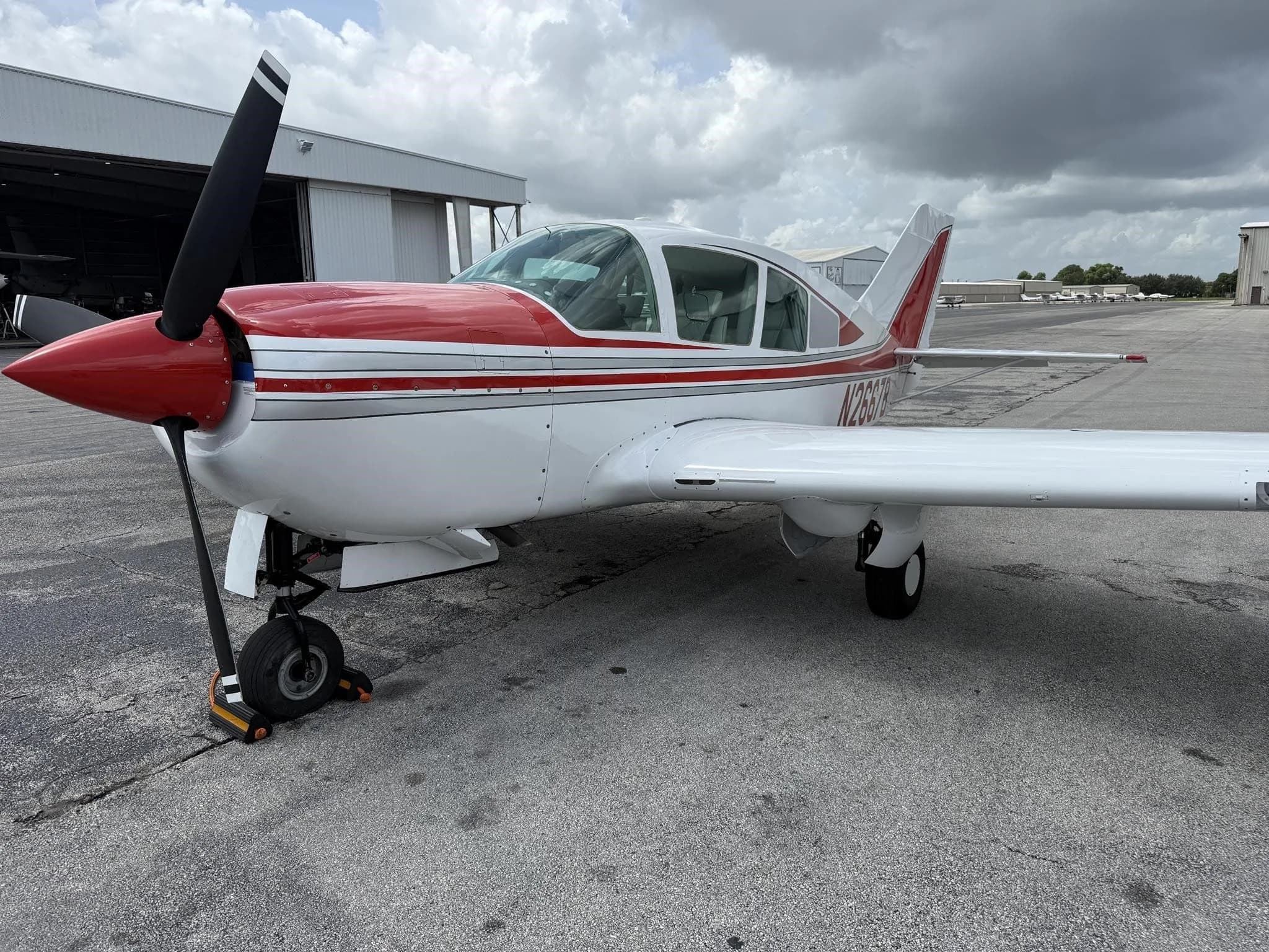 A front-left view of the white and red single-engine aircraft, N2667B, on an airport tarmac.