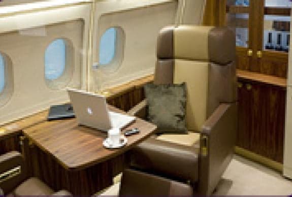 A private jet interior with a desk, laptop, and comfortable chair.