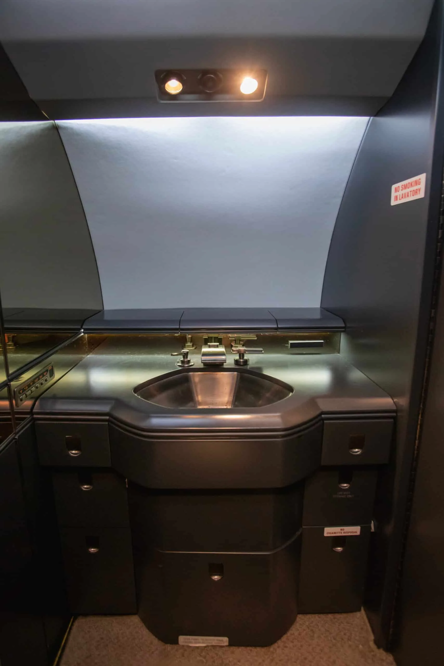 The lavatory of a private jet, featuring a sink, mirror, and "NO SMOKING IN LAVATORY" sign.