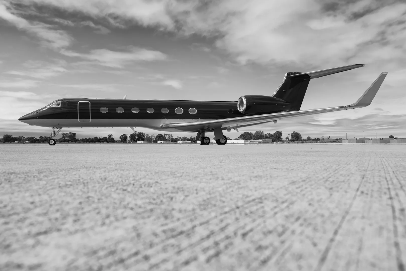 A black and white photo of a sleek private jet parked on an airfield under a cloudy sky.