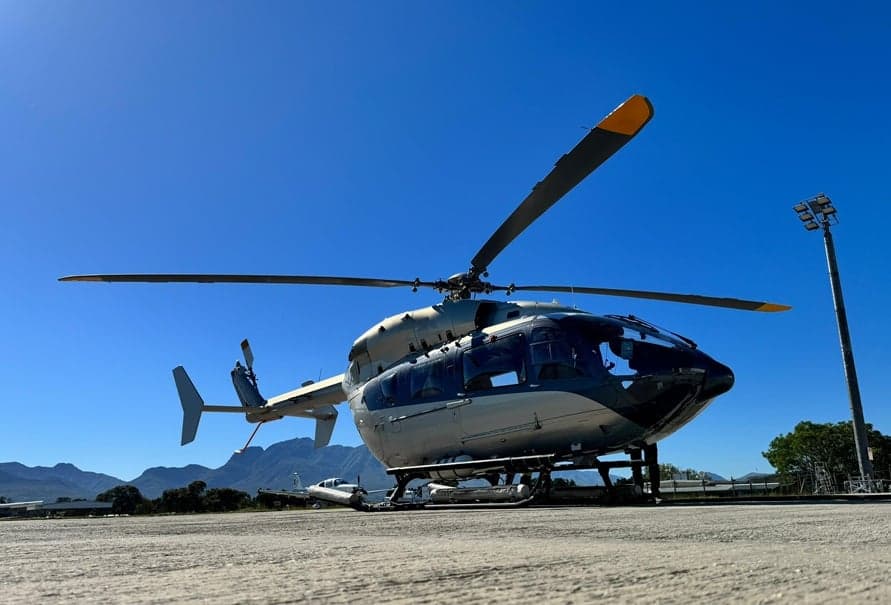 Helicopter parked on the tarmac with mountains in the background.
