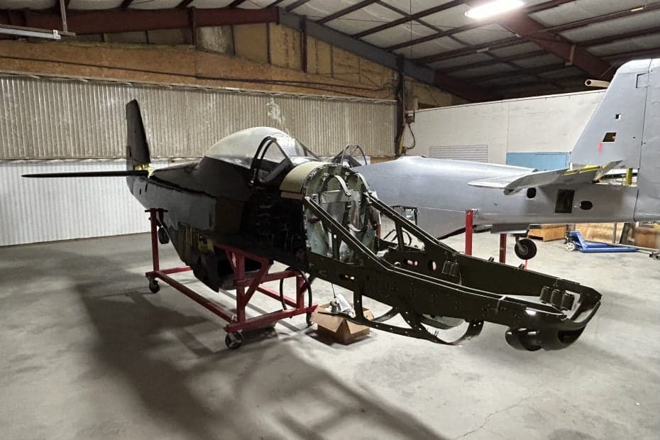 A partially disassembled aircraft fuselage on a rolling stand inside a hangar.