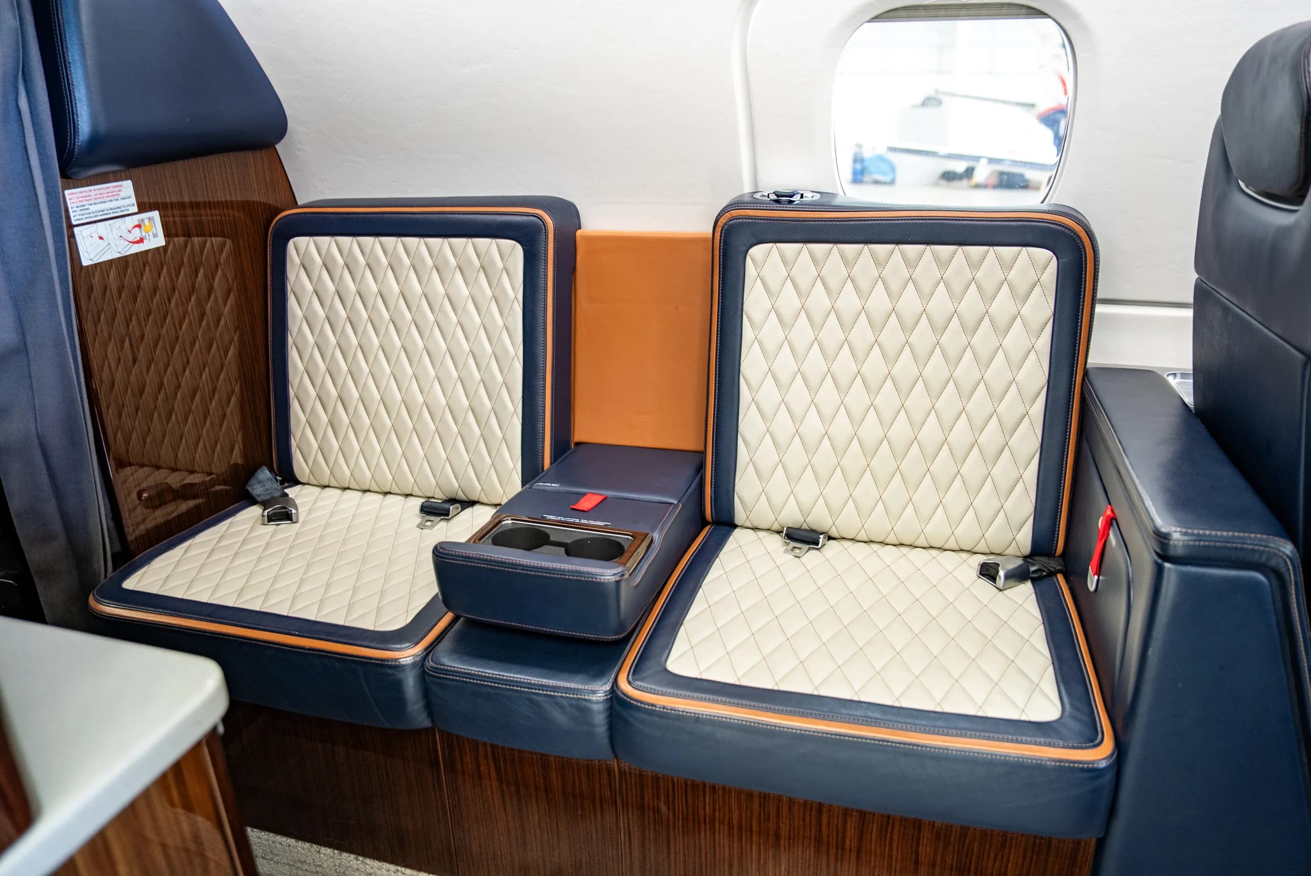A close-up of two dark blue and cream quilted leather seats in the Embraer Phenom 300E cabin, with a central console.
