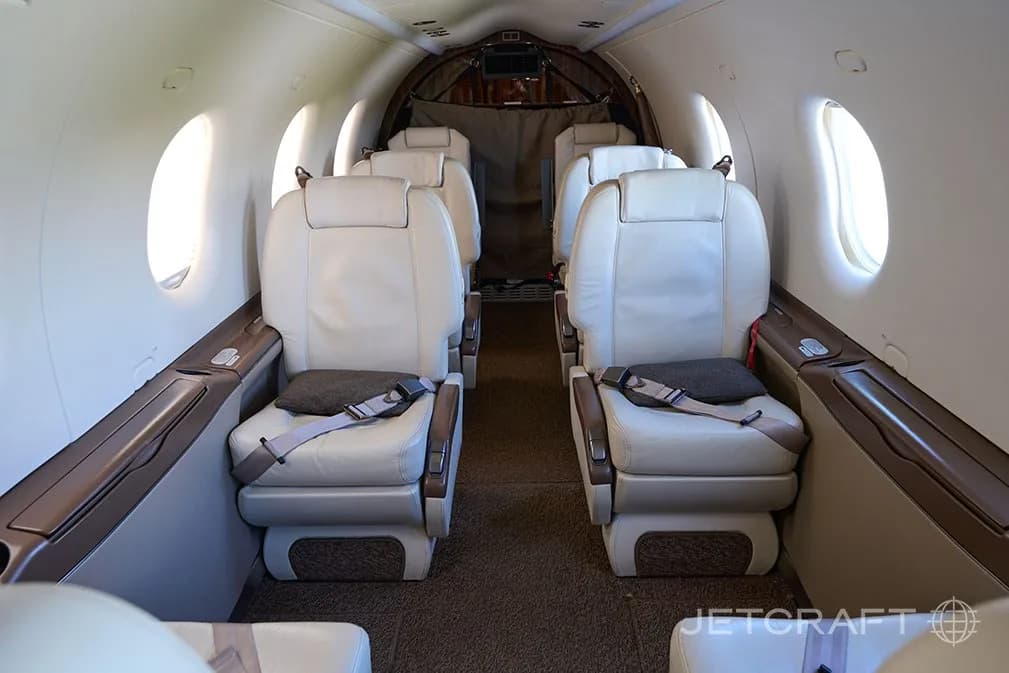 The aircraft cabin interior with light cream leather seats and brown carpet, viewed from the rear.