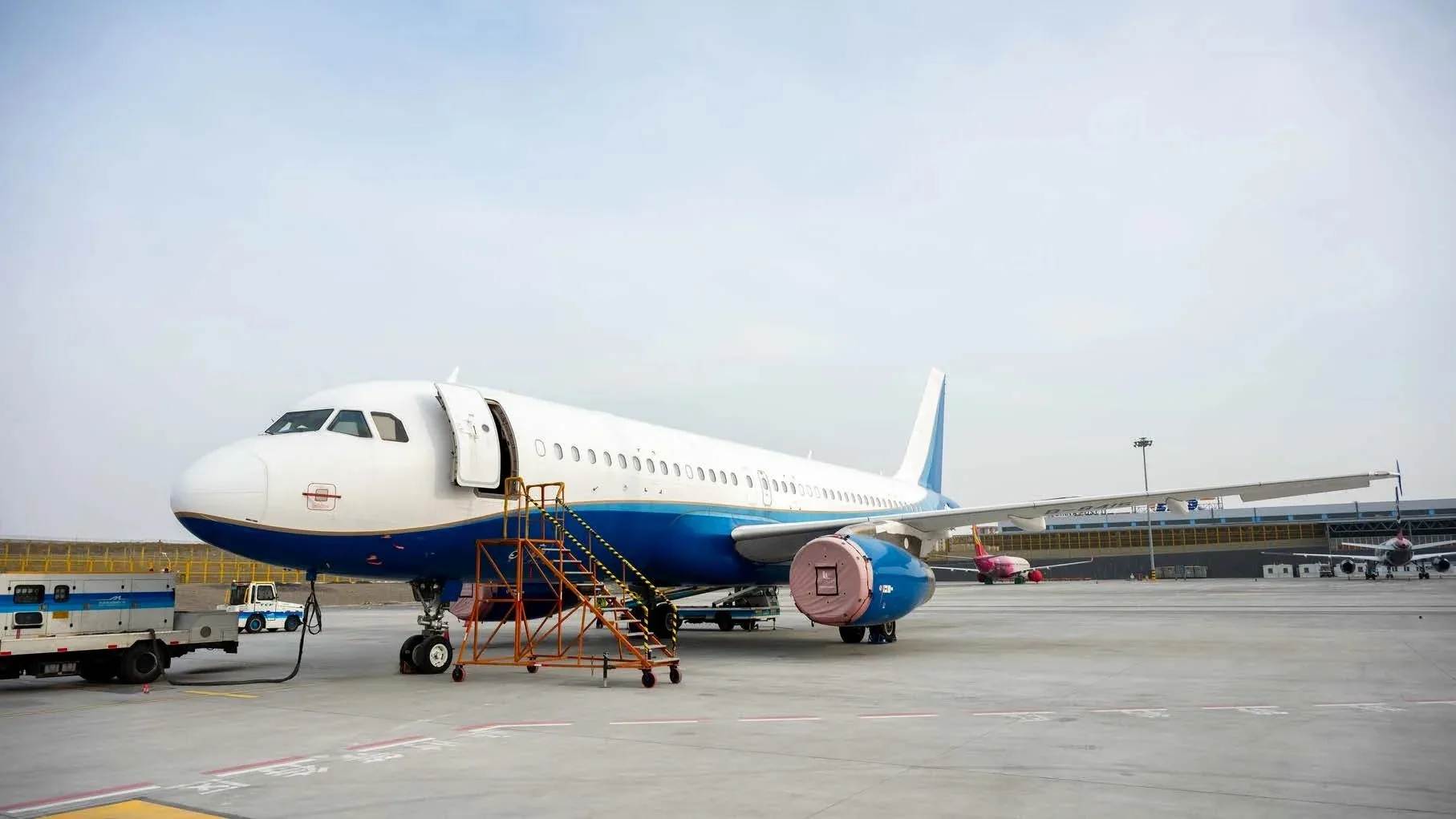 A white and blue Airbus A320 family aircraft parked on the tarmac with an open door and stairs.