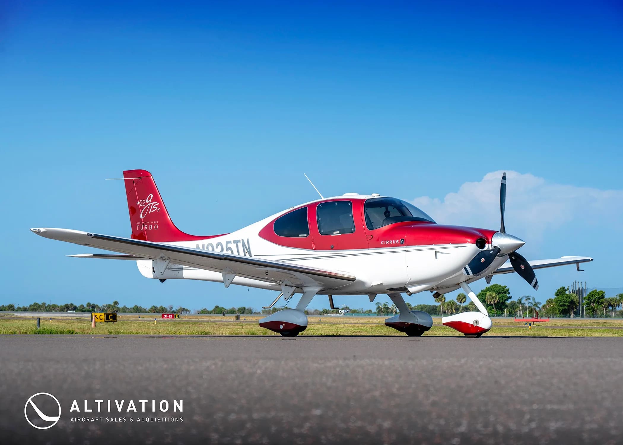 A red and white Cirrus SR22T aircraft (N225TN) parked on an airfield under a clear blue sky.