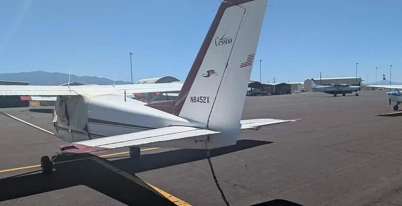 A rear-quarter view of the white and maroon Cessna 172M, N8452X, parked on an airfield.