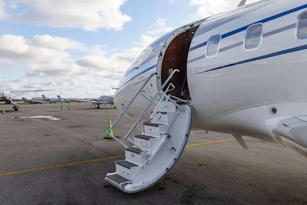 The open main cabin door and integrated airstairs of a white business jet on an airport tarmac.