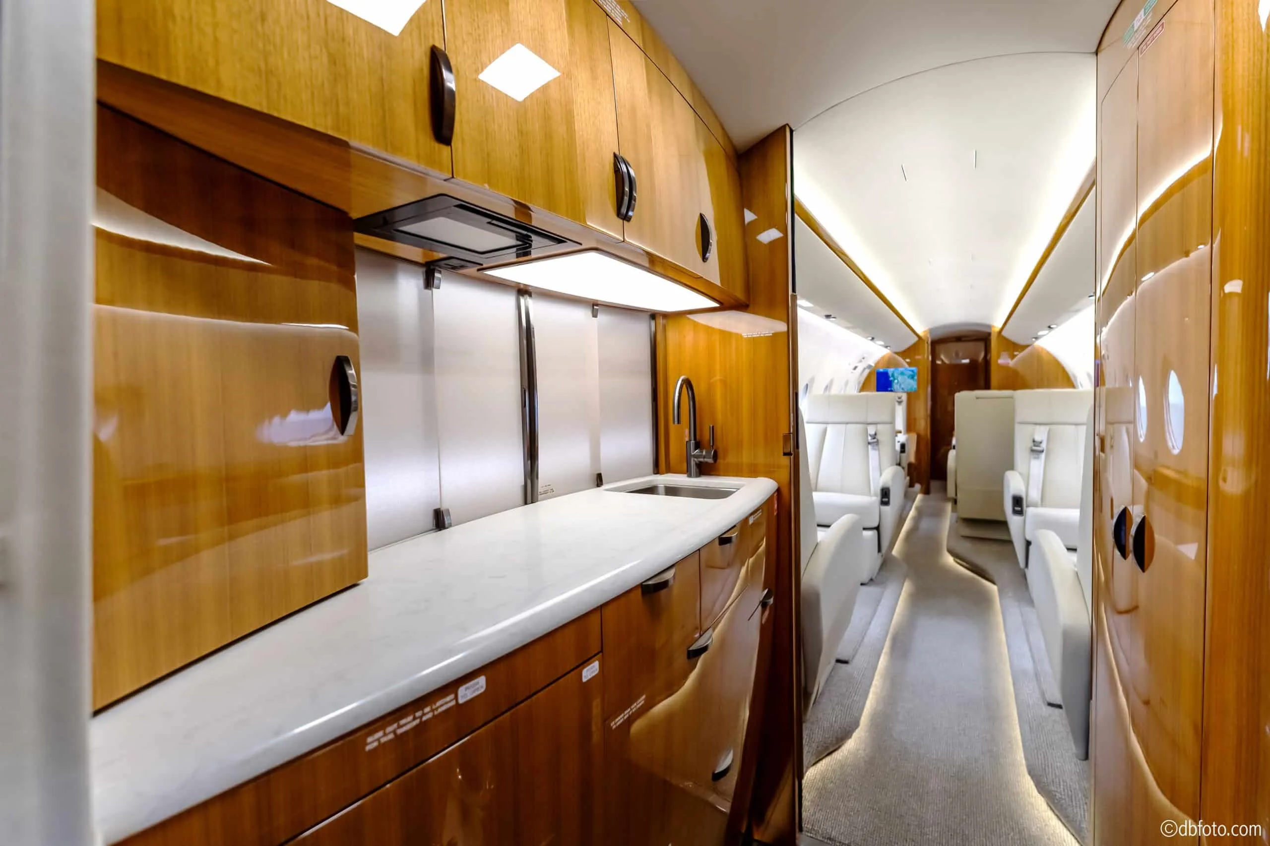 The aircraft's galley with polished wood cabinetry, a sink, and a view into the passenger cabin.