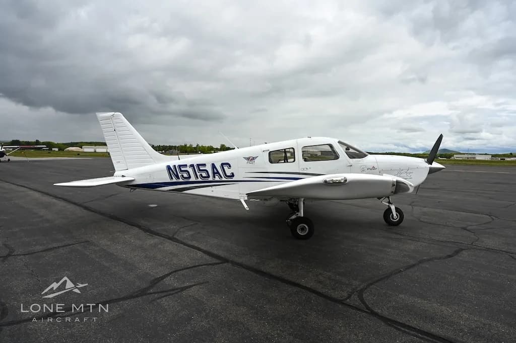 A white single-engine propeller aircraft with blue accents, registration N515AC, parked on an asphalt tarmac under a cloudy sky.