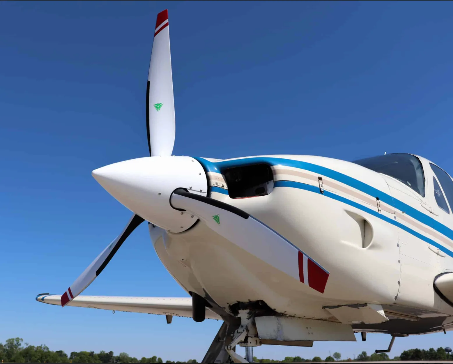 Close-up view of the nose and propeller of a white single-engine aircraft with blue and tan stripes.