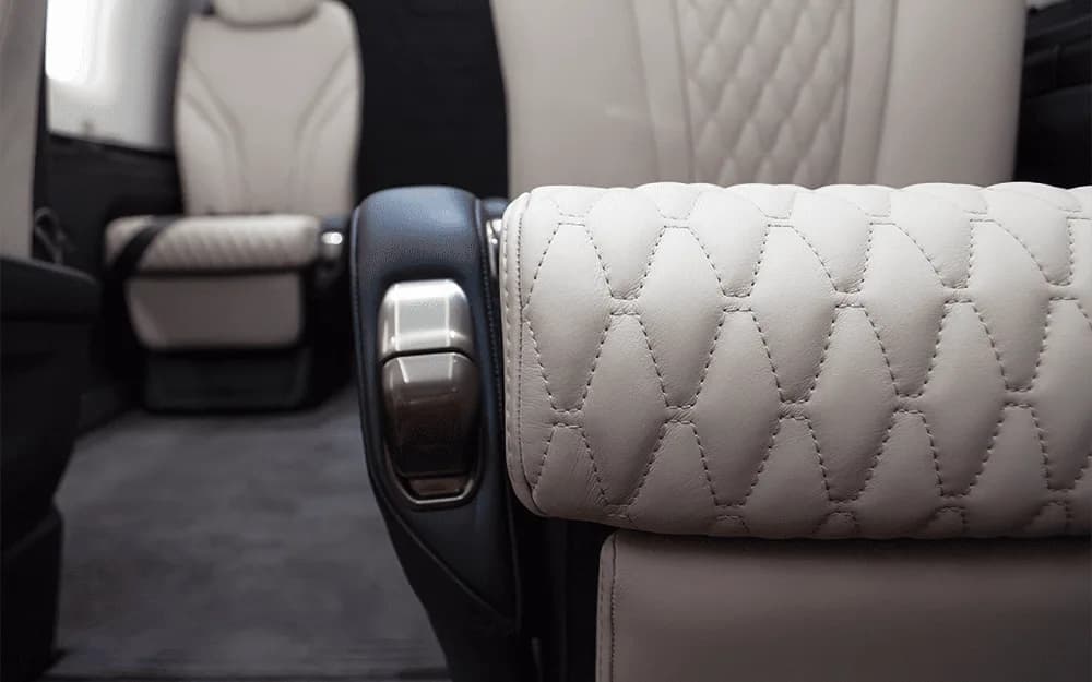 A close-up of the white quilted leather headrest and armrest of a seat in the Pilatus PC-12 NGX cabin.