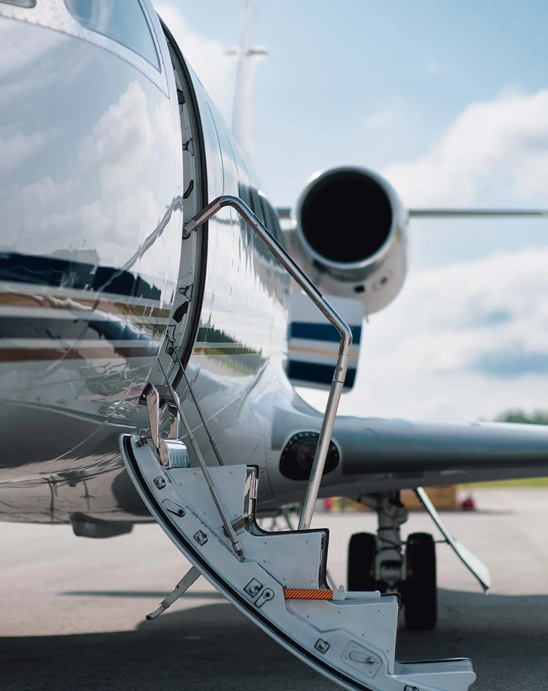 A close-up view of the open main cabin door and airstairs of a white private jet with blue and gold stripes.