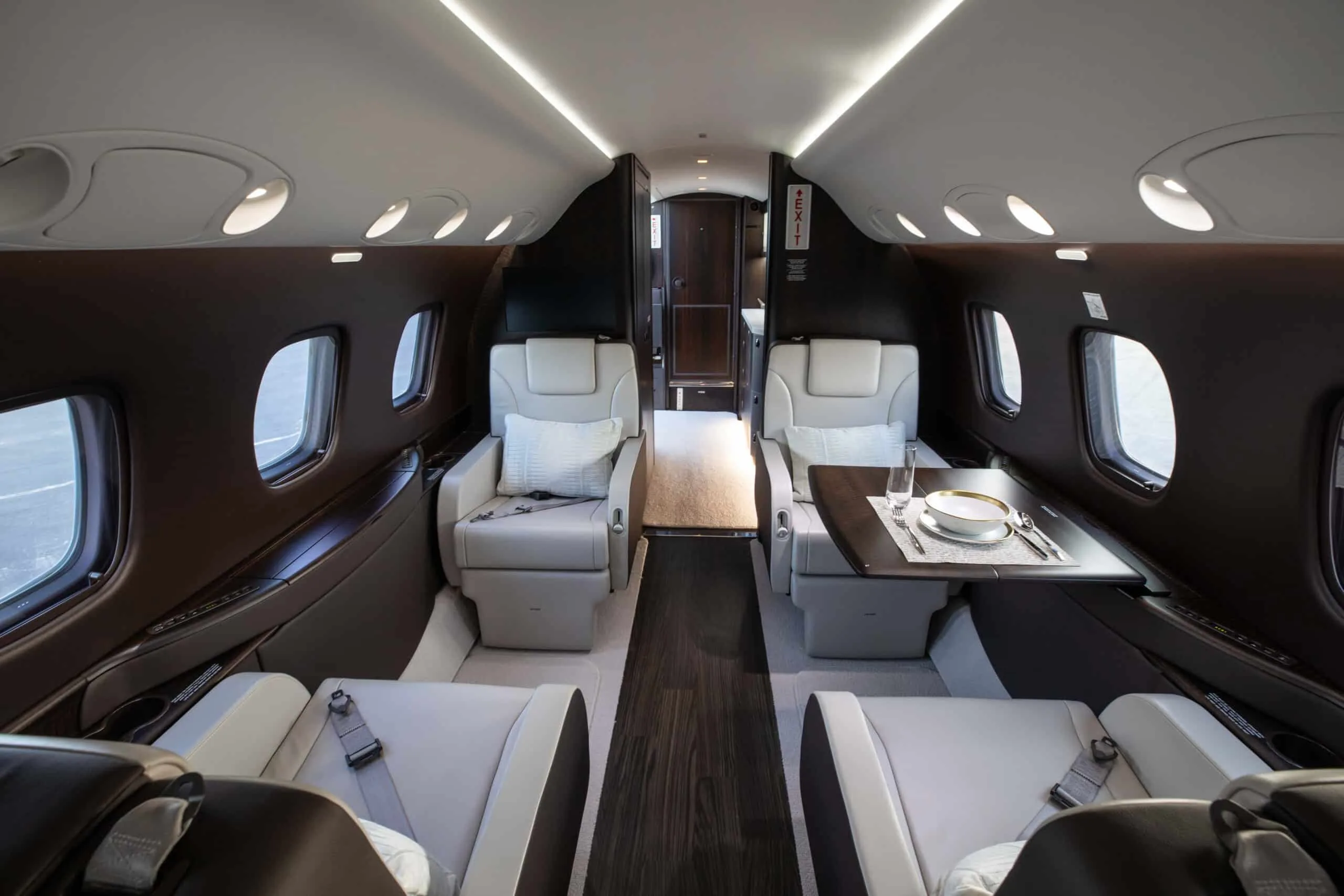 The luxurious interior cabin of the aircraft, featuring light-colored leather seats, a dining table, and dark wood accents.