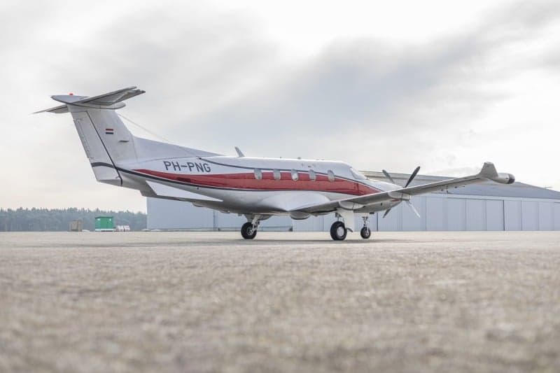 A Pilatus PC-12 aircraft with a silver and red paint scheme, registration PH-PNG, parked on the tarmac.