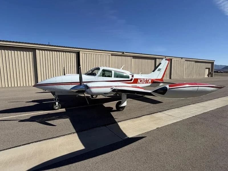 Three-quarter front view of a white and red Cessna 310 twin-engine aircraft with tip tanks parked on an airfield.