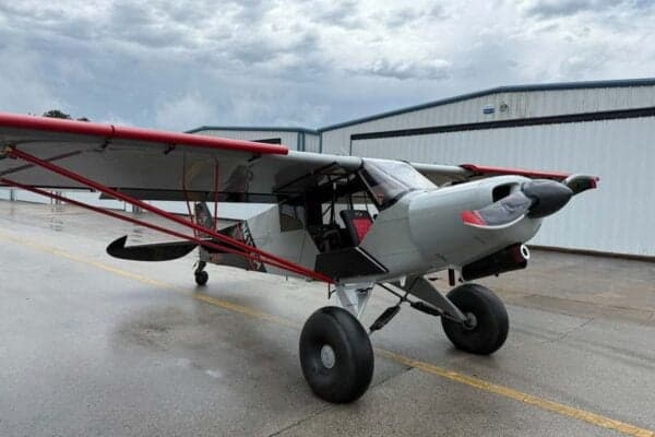 A gray and red N413SM aircraft is parked on the tarmac in front of a hangar on a cloudy day.