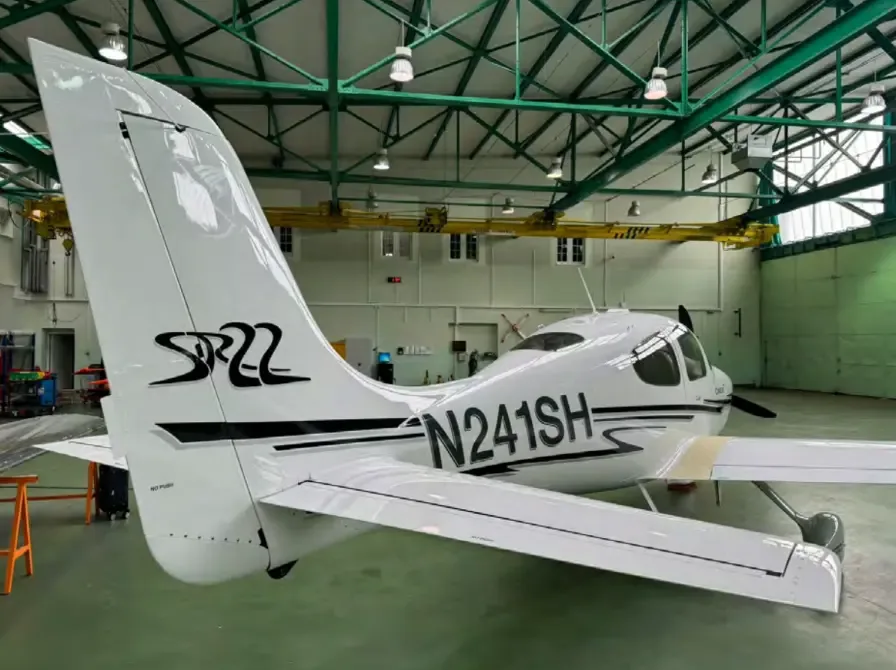A white Cirrus SR22 aircraft with black stripes and registration N241SH, viewed from the rear-left, inside a hangar.