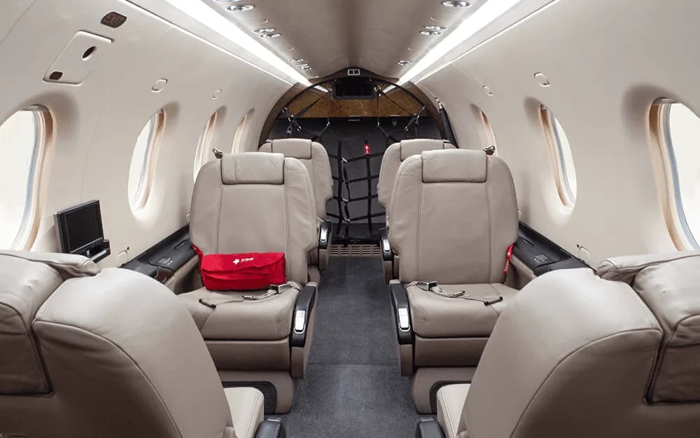 The beige leather interior cabin of a Pilatus PC-12 NG, with a red first aid kit on a seat.